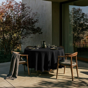 Black Linen Round Tablecloth in a Sunlit Patio Dining Space with Walnut Wood Chairs
