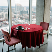 Dark Deep Red Small Velvet Round Tablecloth in a City Dining Room with Floor-To-Ceiling Windows and Rose Upholstery