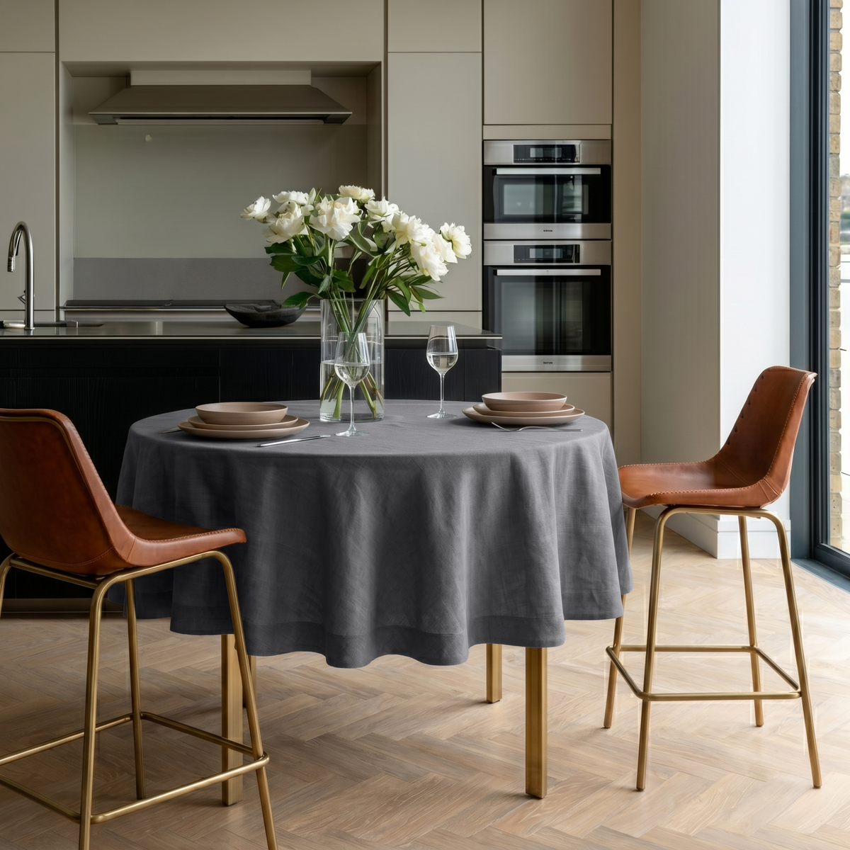 Dim Grey Linen Round Tablecloth in a Modern Kitchen Dining Space with Cream Cabinetry and Tan Leather Chairs