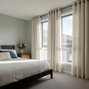 Ecru Heavy Weight Linen Grommet Curtains in a Calm Neutral Bedroom With a Dark Wood Bed and Large Sunlit Windows