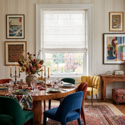 Off-White Roman Shades in a Dining Room with Striped Wallpaper and a Wooden Dining Table and Velvet Dining Chairs