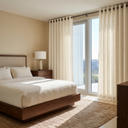 Cream Linen Grommet Curtains in a Warm Neutral Bedroom With a Wooden Bed and Floor-to-Ceiling Windows