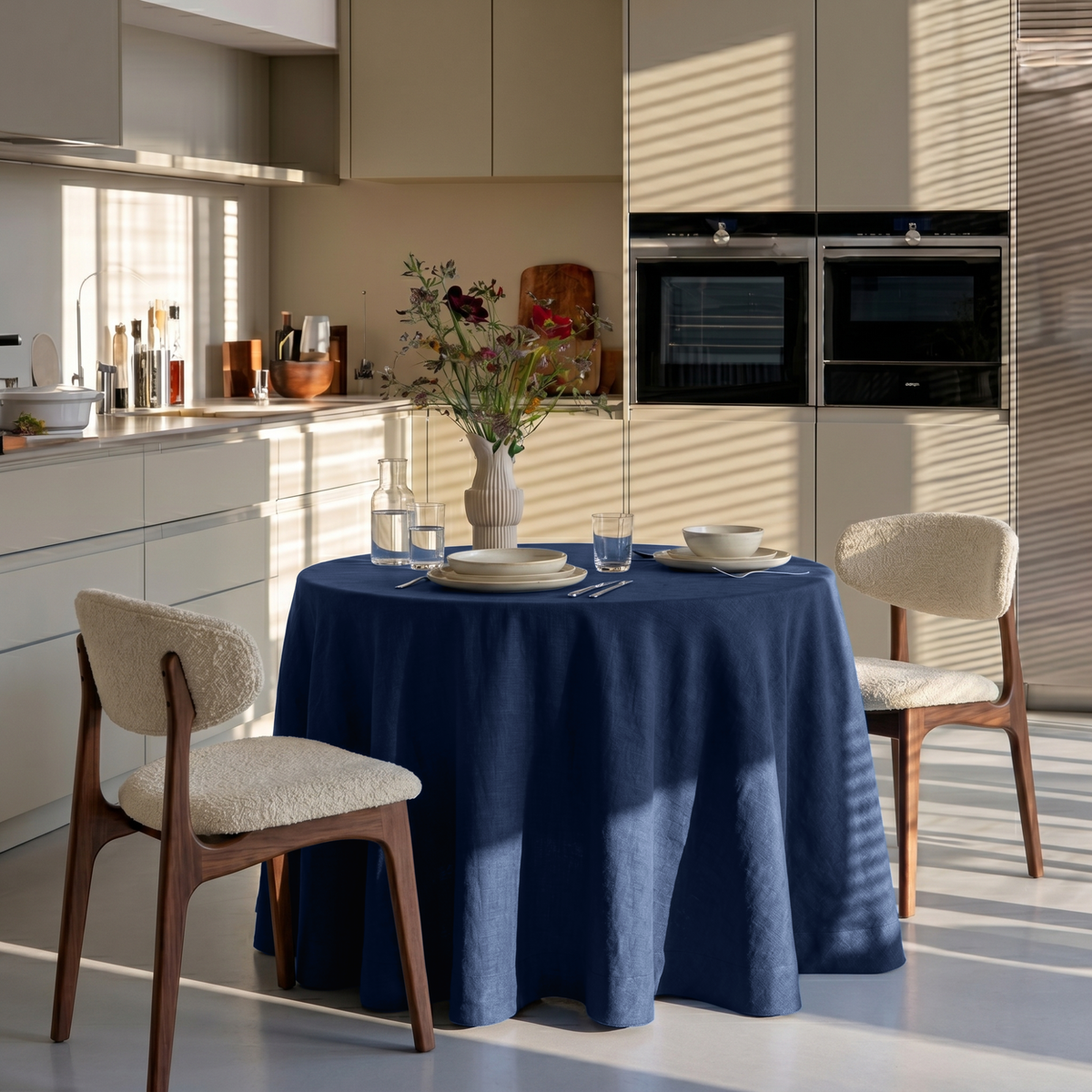Royal Blue Linen Round Tablecloth in a Modern Kitchen Dining Space with Cream Cabinetry and Bouclé Chairs