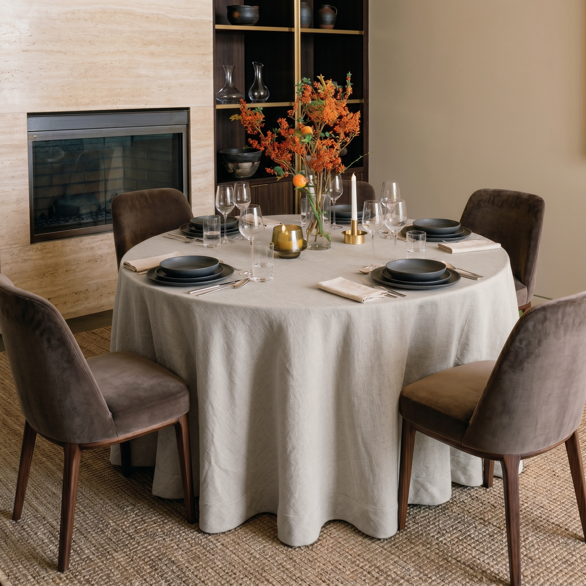 Natural Linen 70 Inch Round Tablecloth in a Warm Dining Room with Travertine Fireplace and Brown Velvet Chairs