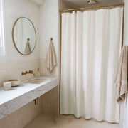 Off-White Linen Button-Hole Top Shower Curtain in a Minimal Bathroom with Beige Stone Walls and Marble Vanity