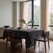 Charcoal Grey Rectangular Linen Tablecloth in a Modern Dining Room with Floor-to-Ceiling Windows and Woven Leather Chairs