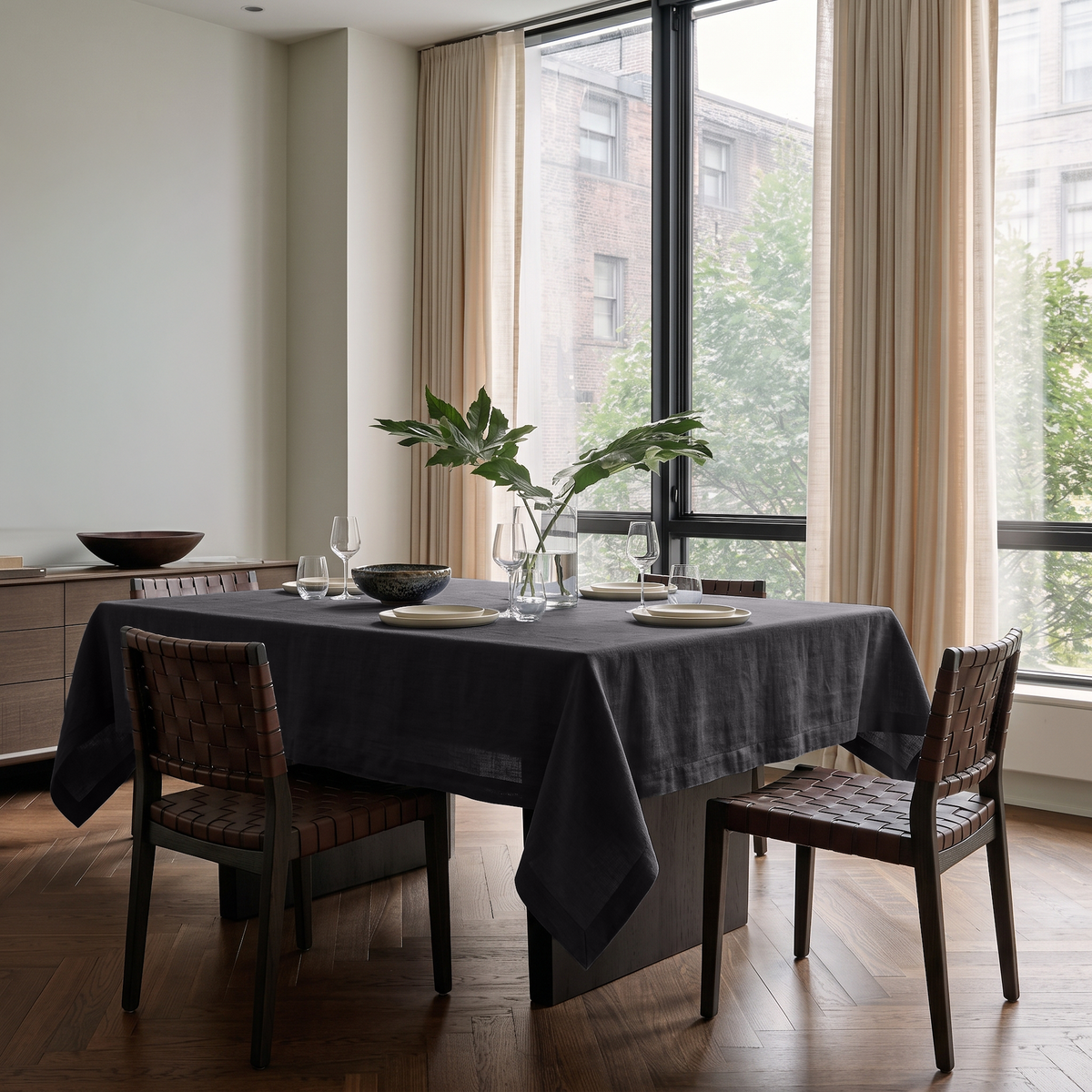 Charcoal Grey Rectangular Linen Tablecloth in a Modern Dining Room with Floor-to-Ceiling Windows and Woven Leather Chairs