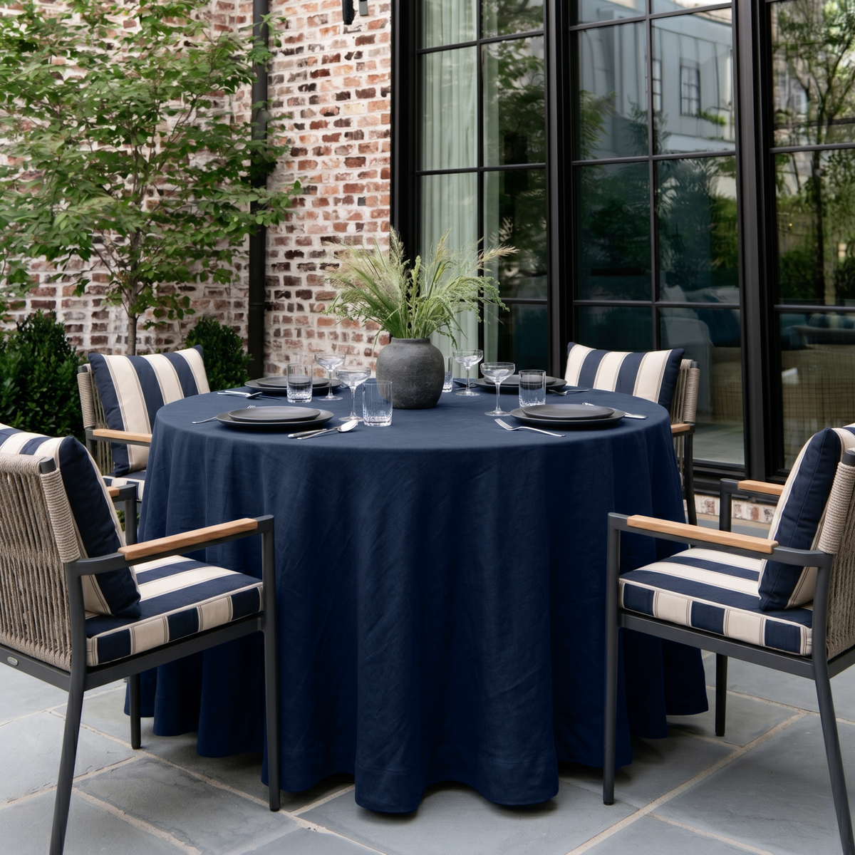 Royal Blue Linen 70 Inch Round Tablecloth in a Patio Dining Space with Brick Walls and Navy Striped Accents