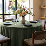 Sage Green Linen 70 Inch Round Tablecloth in a Sunlit Dining Room with Soft Beige Walls and Taupe Velvet Chairs