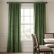 A calm traditional dining room with floor-length sage-green curtains, a large white-framed window, classic wooden chairs with beige upholstery, and soft natural light