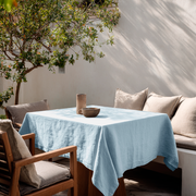 Sky Blue Square Linen Tablecloth on a Bright Outdoor Patio with Wood-Framed Seating and Neutral Cushions