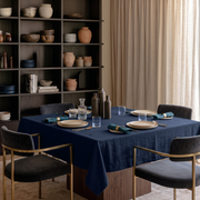 Royal Blue Square Linen Tablecloth in a Modern Dining Room with Dark Built-In Shelving and Cream Curtains