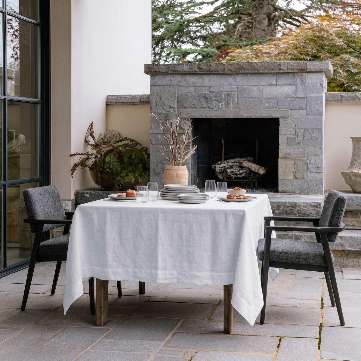 White Square Linen Tablecloth in a Contemporary Outdoor Patio with Stone Fireplace and Gray Armchairs