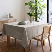 Natural Square Linen Tablecloth in a Bright Modern Dining Room with Cane Chairs and Indoor Greenery