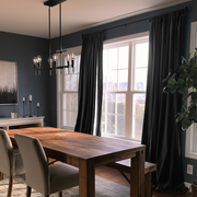 A stylish dining room with charcoal walls, floor-length black curtains, a large wooden table, upholstered chairs, modern pendant lighting, and abundant natural light