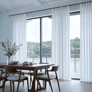 White Linen S-Fold Dining Room Curtain in a Modern Minimalist Dining Room with Light Blue-Grey Walls, a Sleek Wooden Table and a Waterfront View.